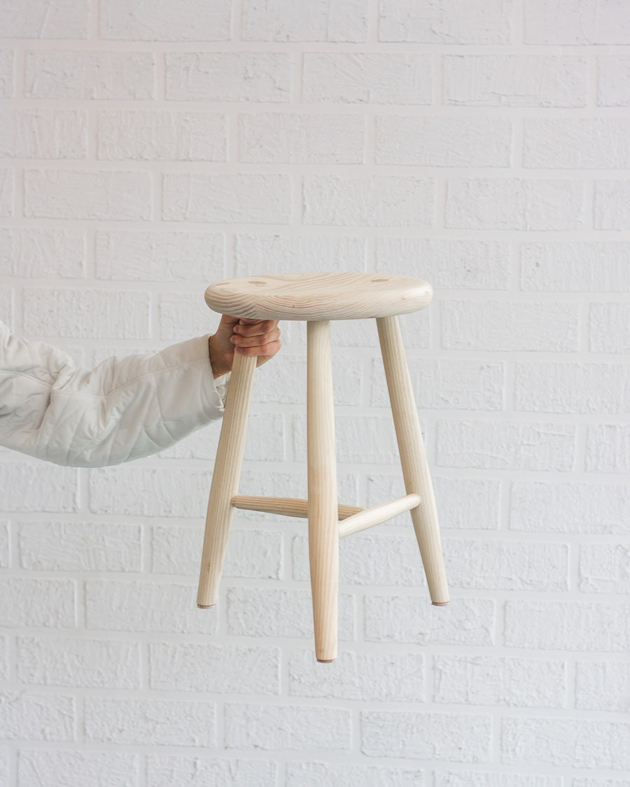 Wooden stool held by a person against a white brick wall