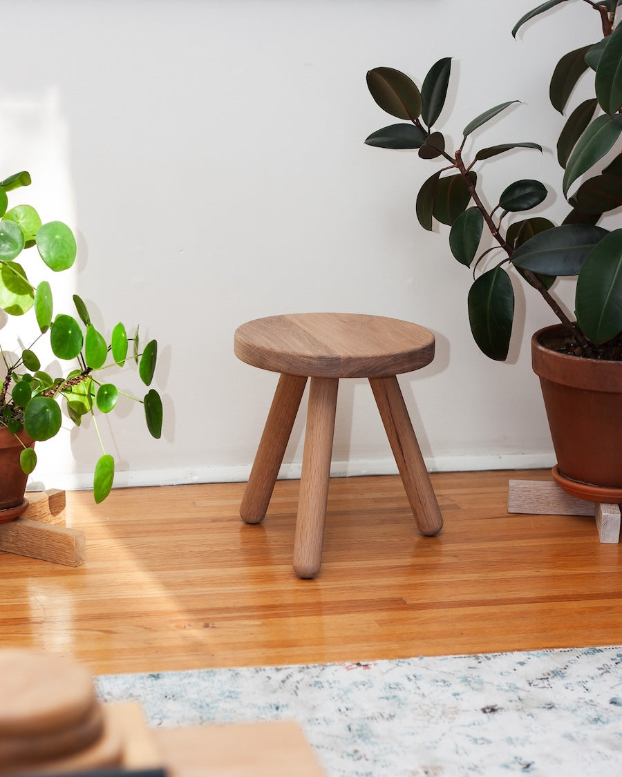 Wooden stool in a room with plants and a light-colored floor.