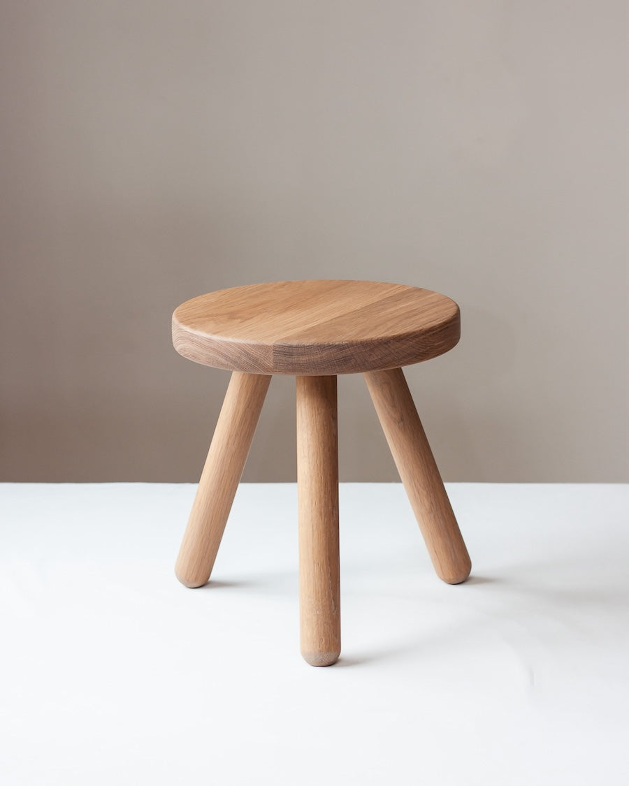 Wooden stool with three legs on a white surface against a beige background
