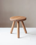 Wooden stool with three legs on a white surface against a beige background