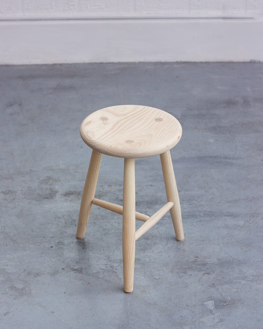 Wooden stool on a gray concrete floor with a white wall background