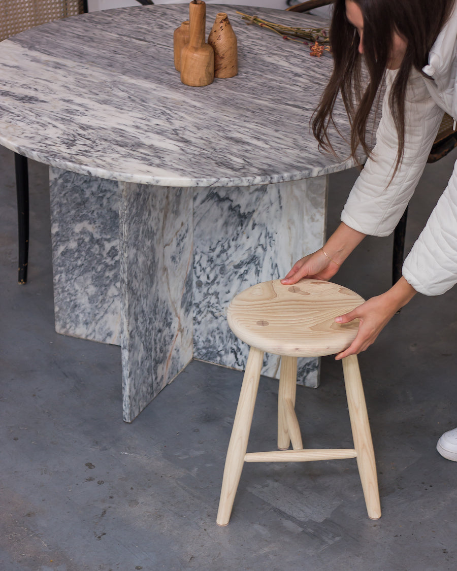 Person holding a wooden stool next to a marble table