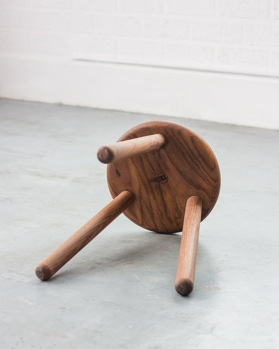 Wooden stool with three legs on a light gray surface