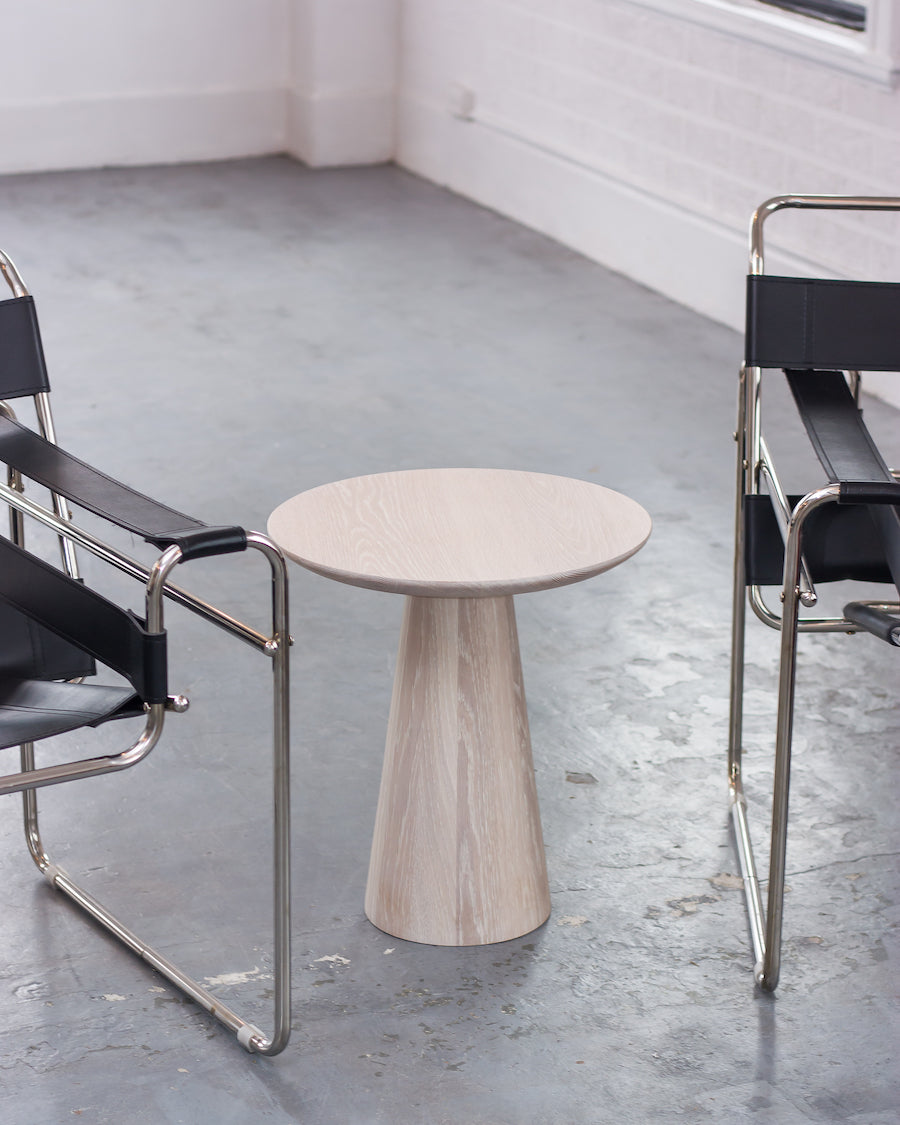 Round wooden table with a cylindrical base in a minimalistic room.