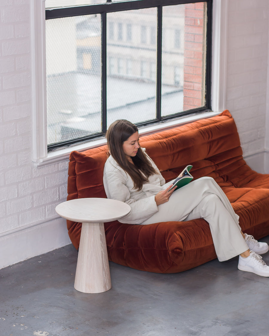 Woman reading a book on a rust-colored sofa in a modern room with large windows.