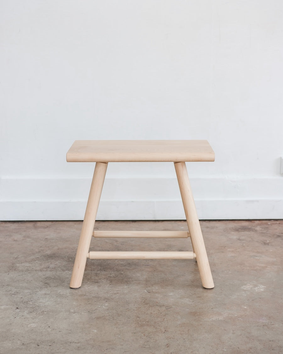 Wooden stool against a white wall on a wooden floor