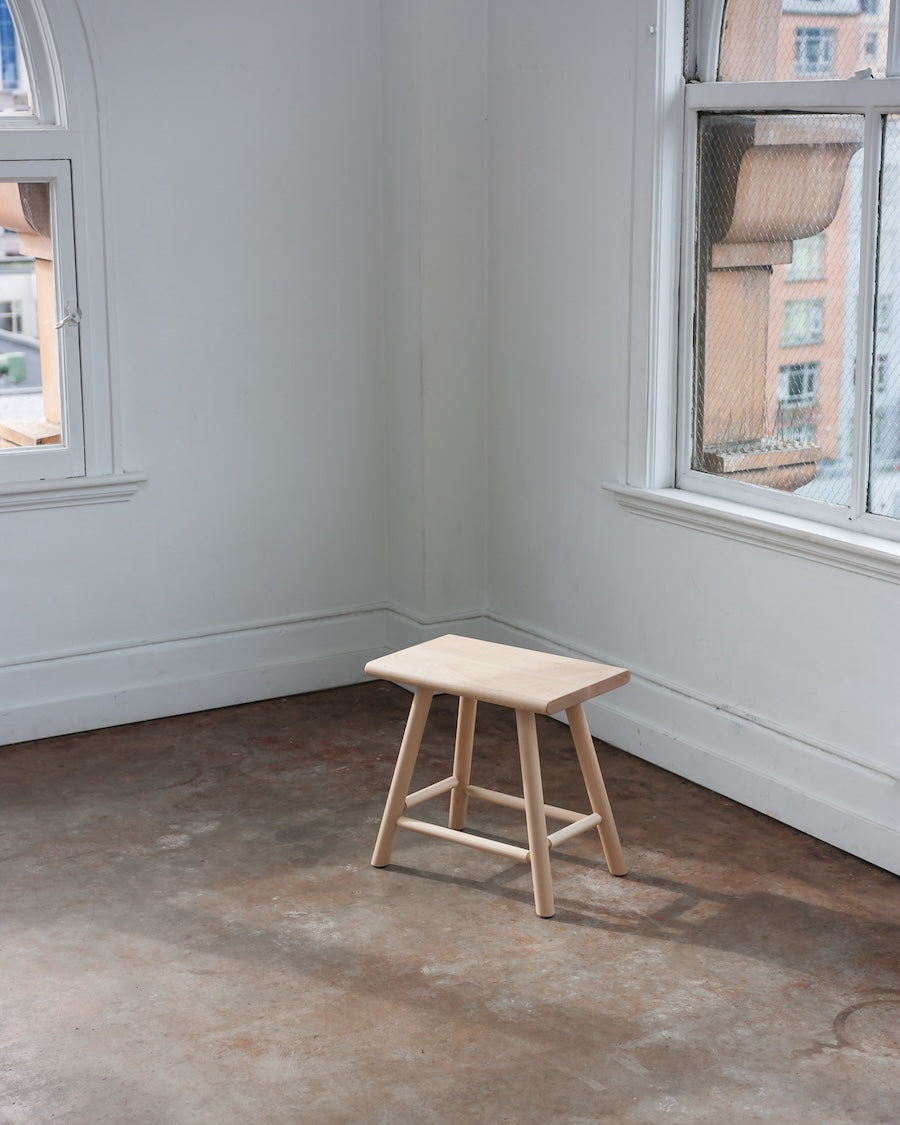 Wooden stool in a room with concrete floor and large windows.