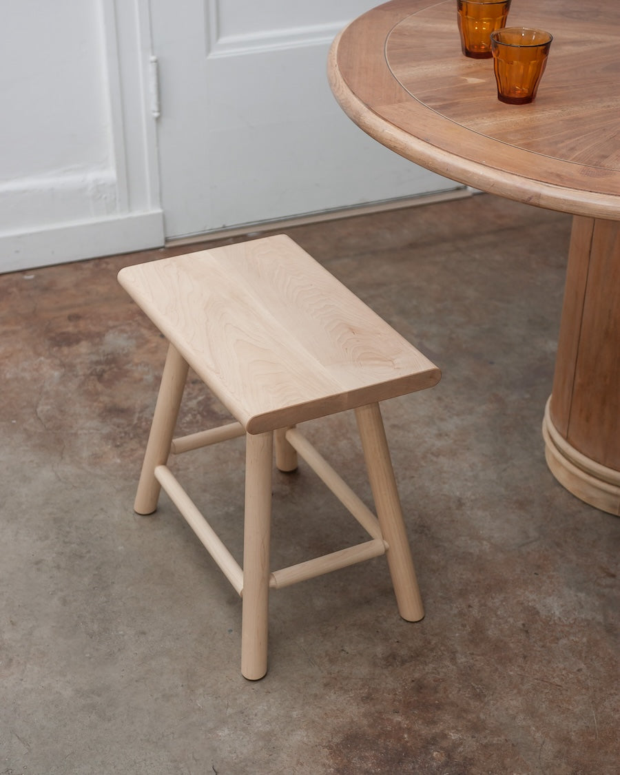Wooden stool in front of a wooden table with glasses on a concrete floor.