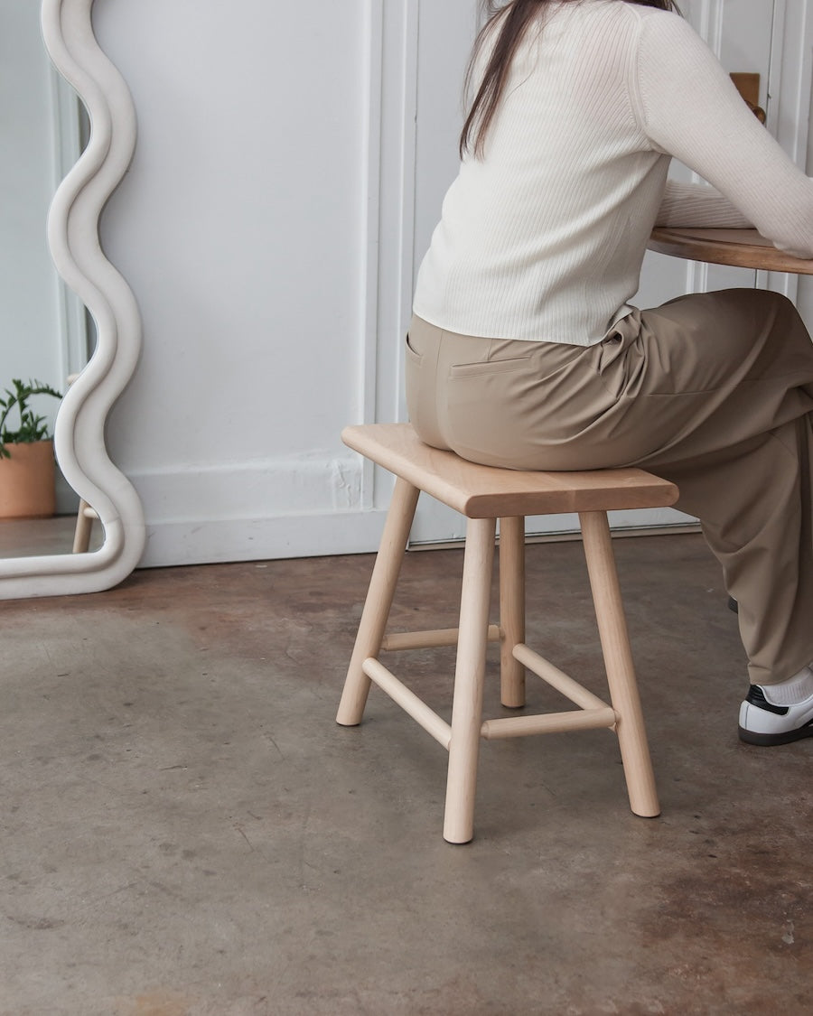Person sitting on a wooden stool in a minimalistic room.