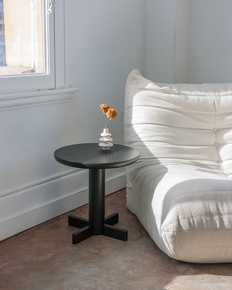 Black side table with a small decorative vase and flowers next to a white sofa.