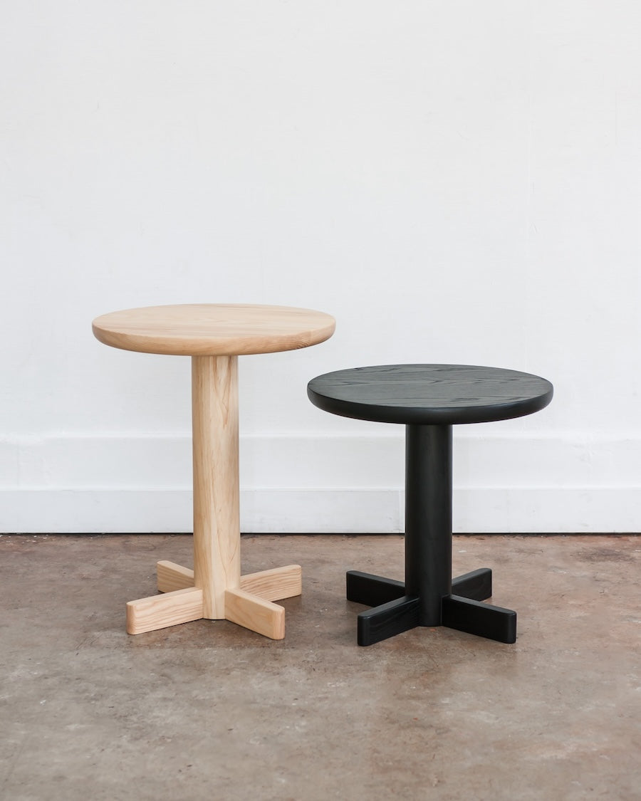 Two round stools, one wooden and one black, on a concrete floor with a white wall background.