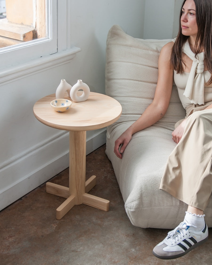 Woman sitting on a beige sofa next to a small wooden table with decorative items.