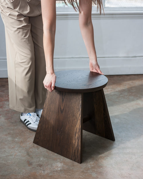 Person lifting a wooden stool with a neutral background