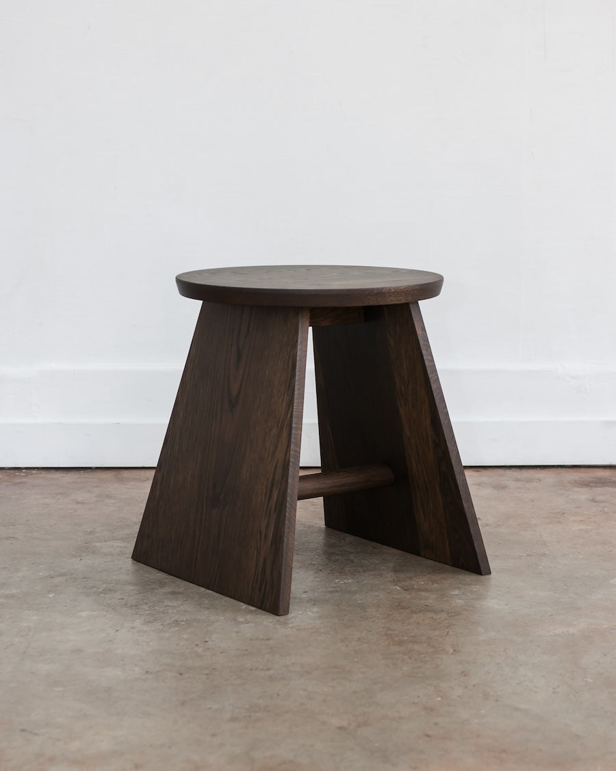 Wooden stool with a round top on a concrete floor against a white wall