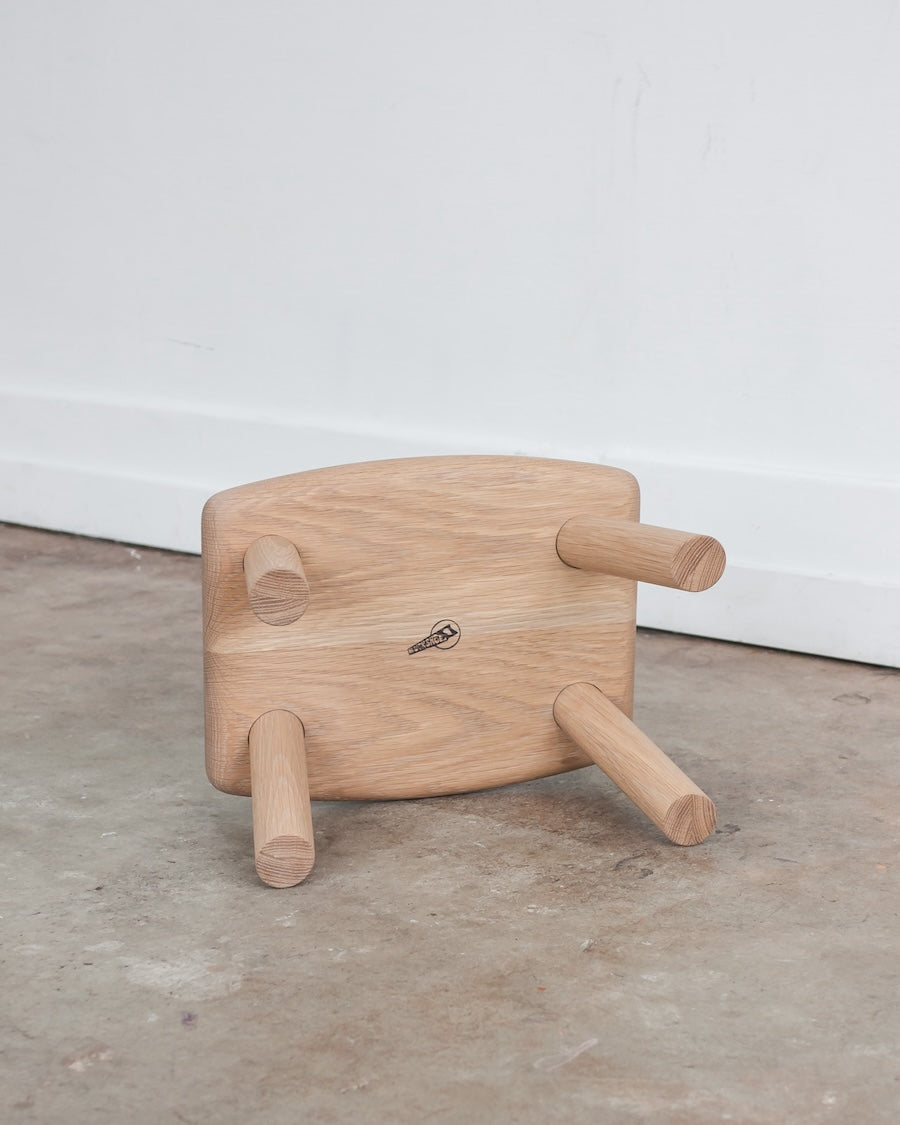 Wooden stool with three legs on a concrete floor against a white wall