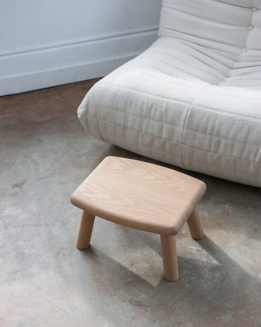 Wooden stool on a concrete floor with a white sofa in the background