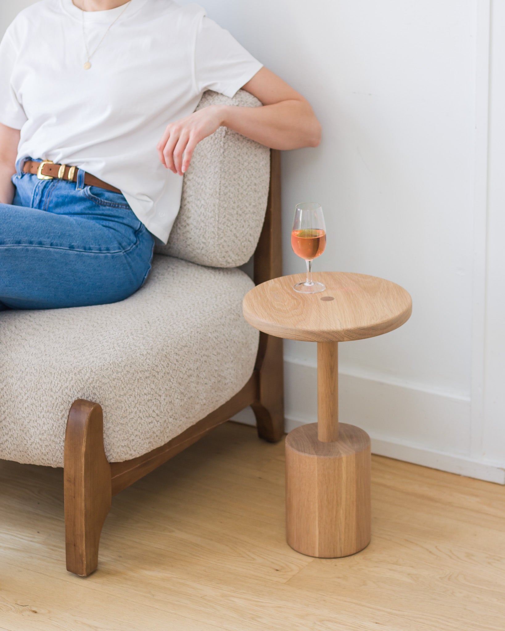 Person sitting on a beige armchair next to a small wooden side table with a glass of wine.