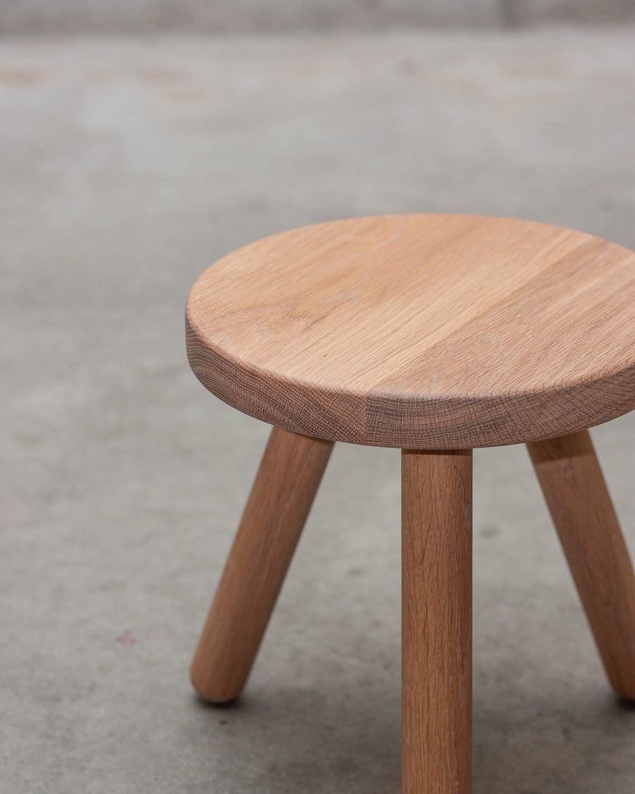 Wooden stool with a round top and four legs on a concrete floor.