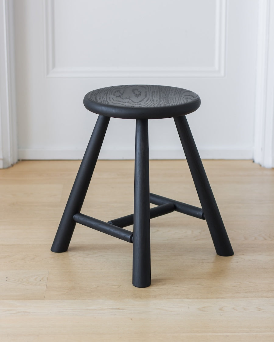 Black stool on a wooden floor with a white paneled wall in the background