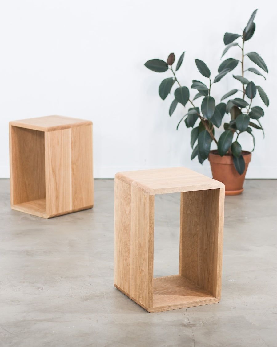 Two wooden side tables on a concrete floor with a plant in the background.