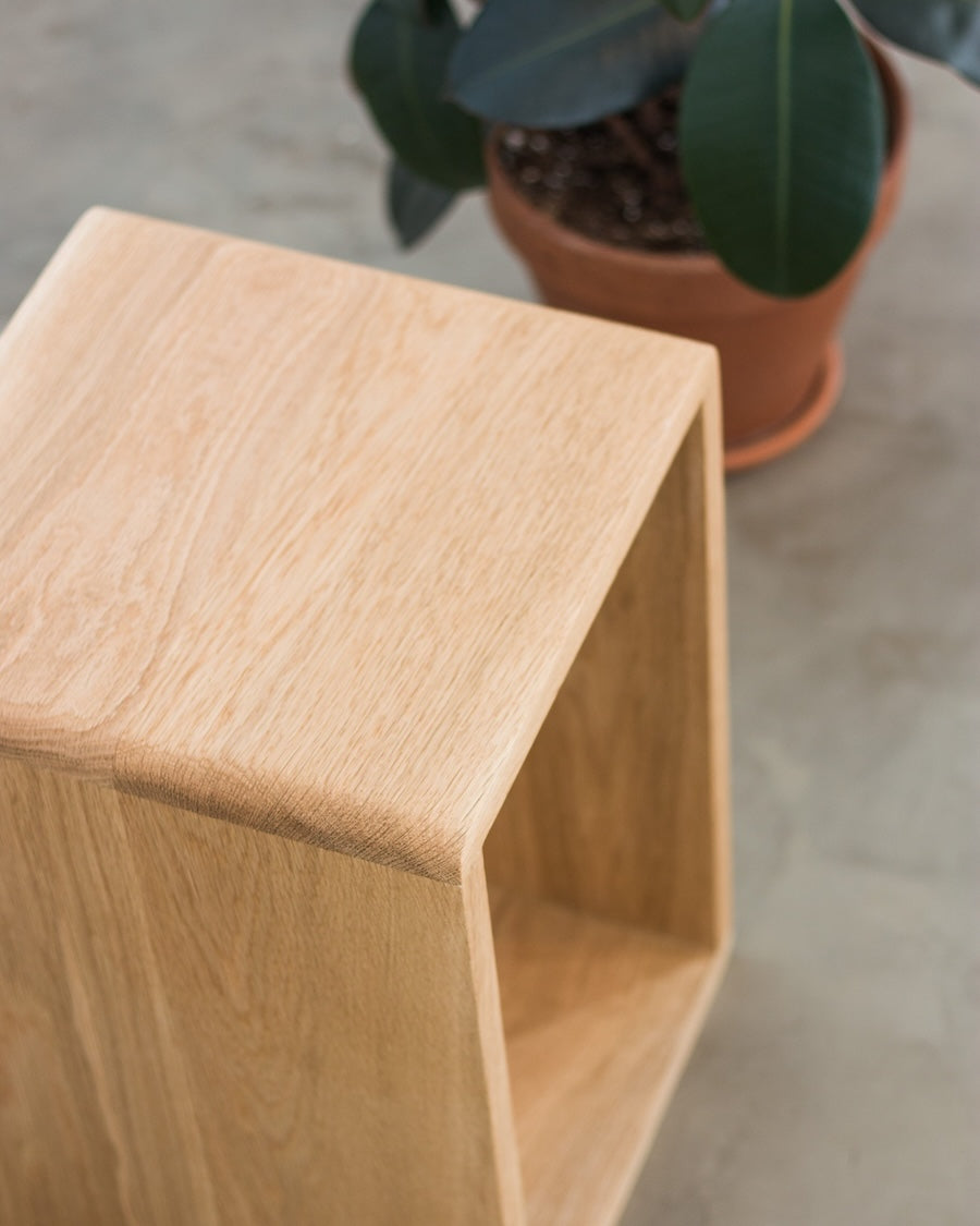 Wooden cube with a potted plant in the background on a concrete floor