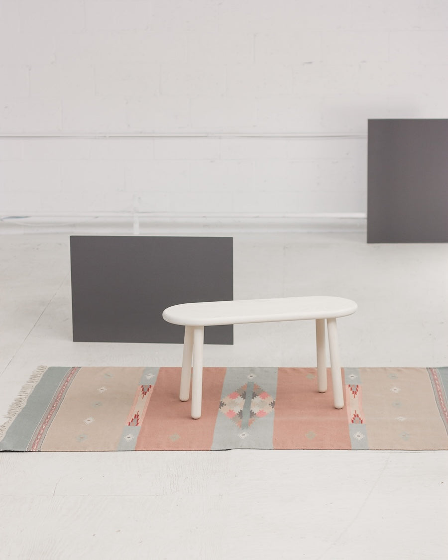 White oval table on a colorful rug with gray walls and a light floor.