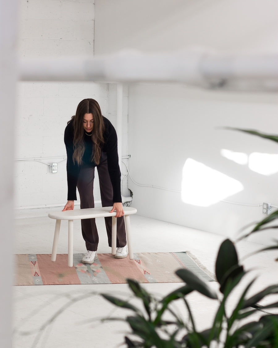 Person adjusting a small table in a minimalistic room with plants.