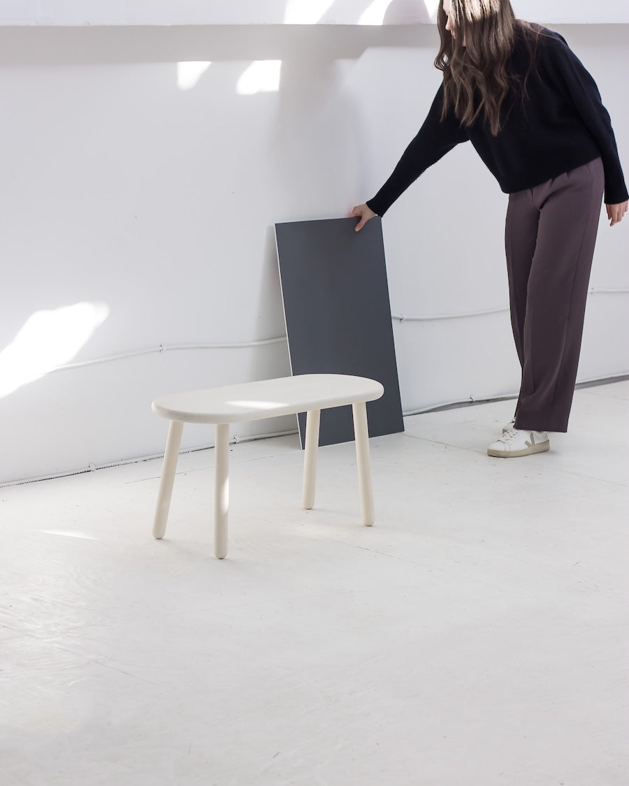 Person holding a dark gray panel next to a white bench in a minimalistic setting