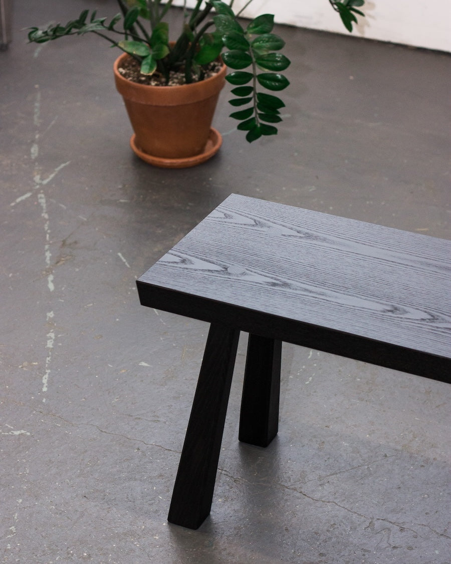 Black wooden bench on a concrete floor with a potted plant in the background