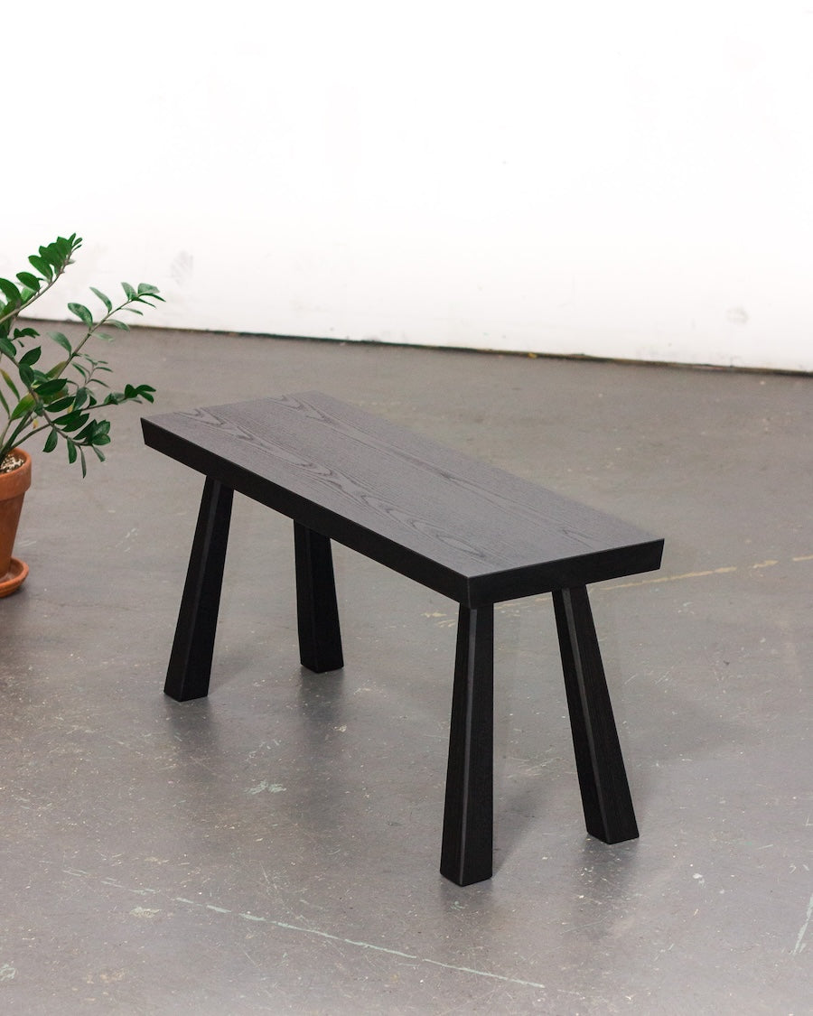 Black wooden bench on a gray floor with a white wall in the background
