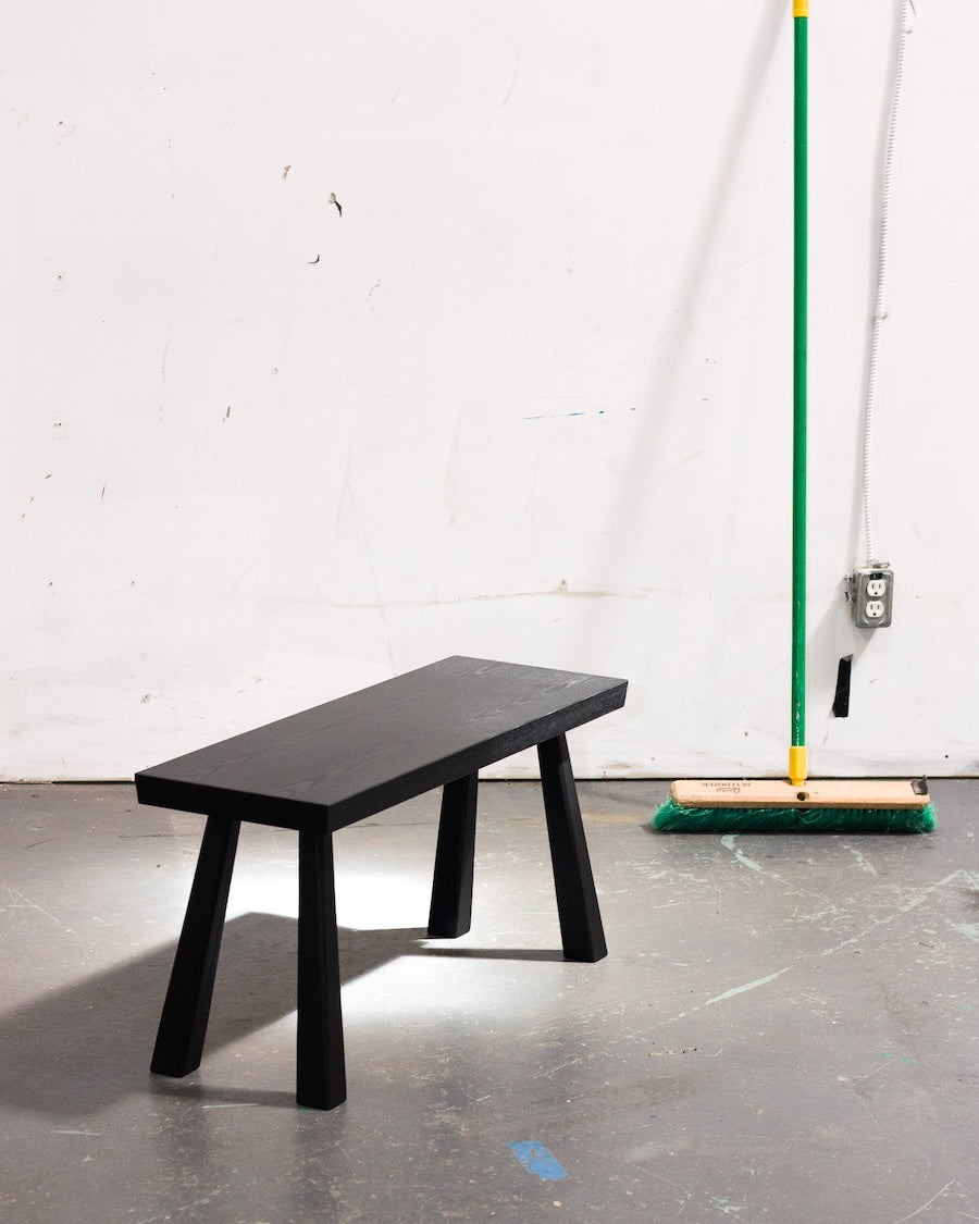 Black bench against a white wall with cleaning equipment in the background