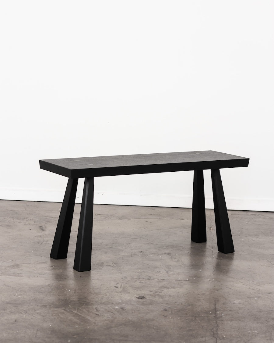 Black dining table with minimalist design on a gray floor.