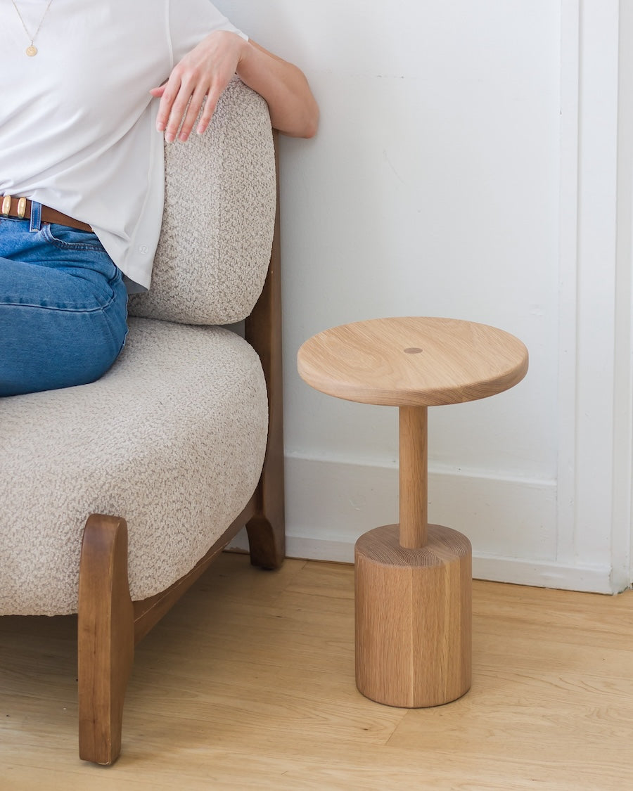 Wooden side table next to a chair with a person sitting on it.