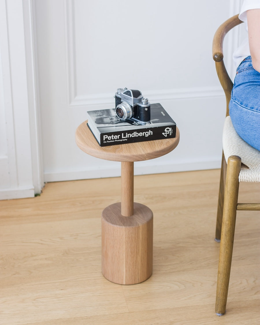 Small wooden side table with a book and camera on top, next to a chair.