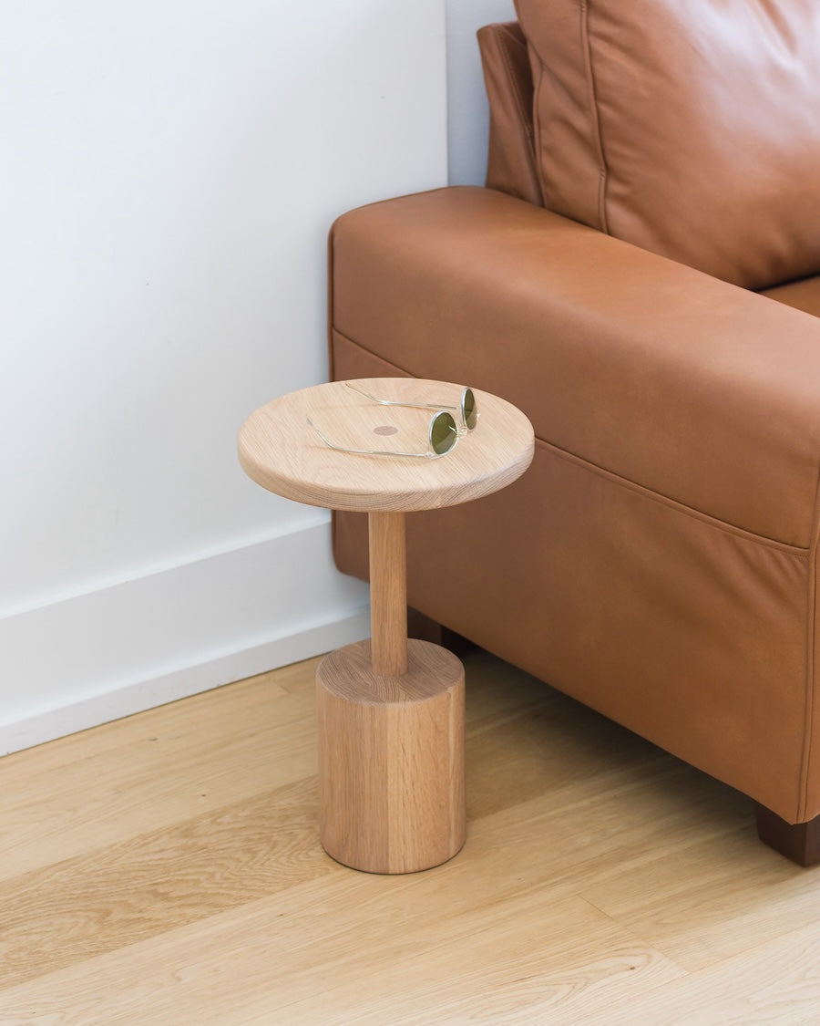 Wooden side table next to a brown leather sofa on a wooden floor.