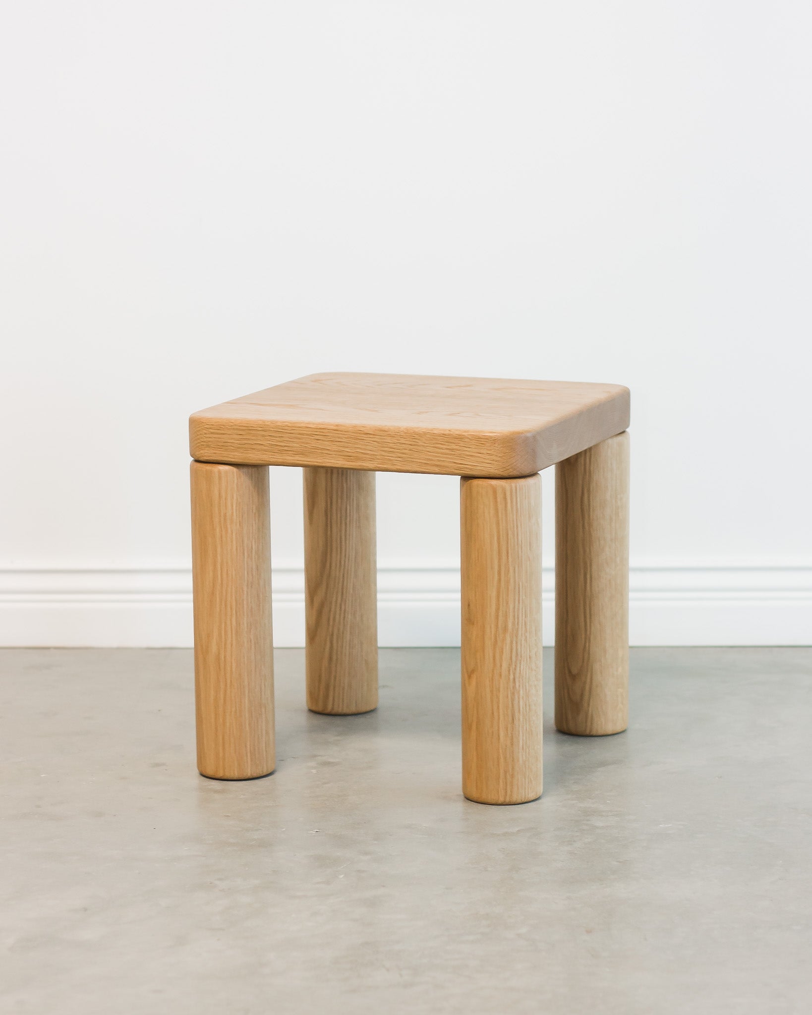 Wooden stool with a square seat and cylindrical legs on a plain background
