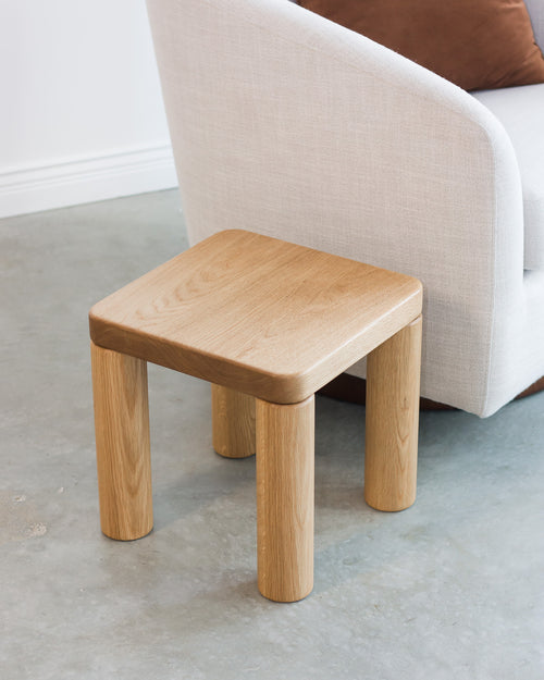 Wooden stool in front of a sofa on a concrete floor