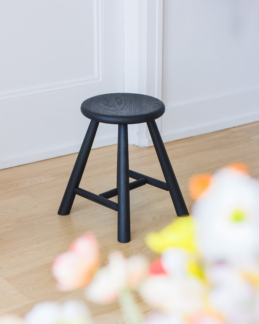 Black stool on a wooden floor with a blurred floral arrangement in the foreground