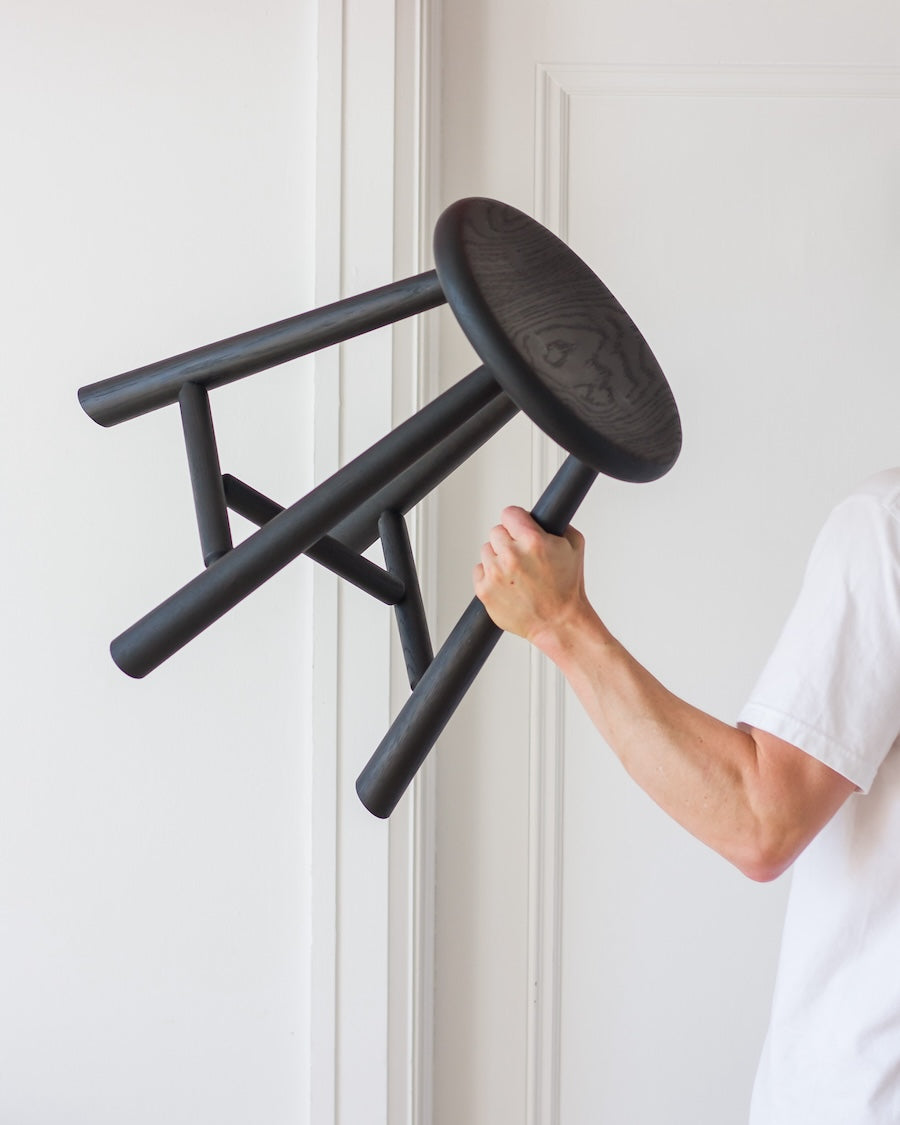 Person holding a black stool against a white wall