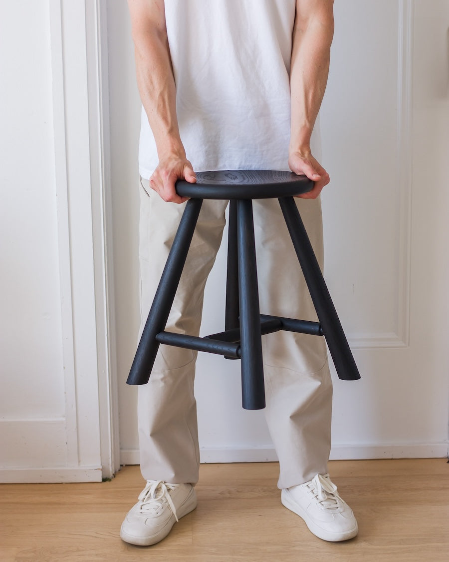 Person holding a black stool against a white wall