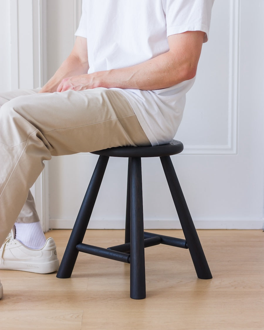 Person sitting on a black stool in a minimalistic room.