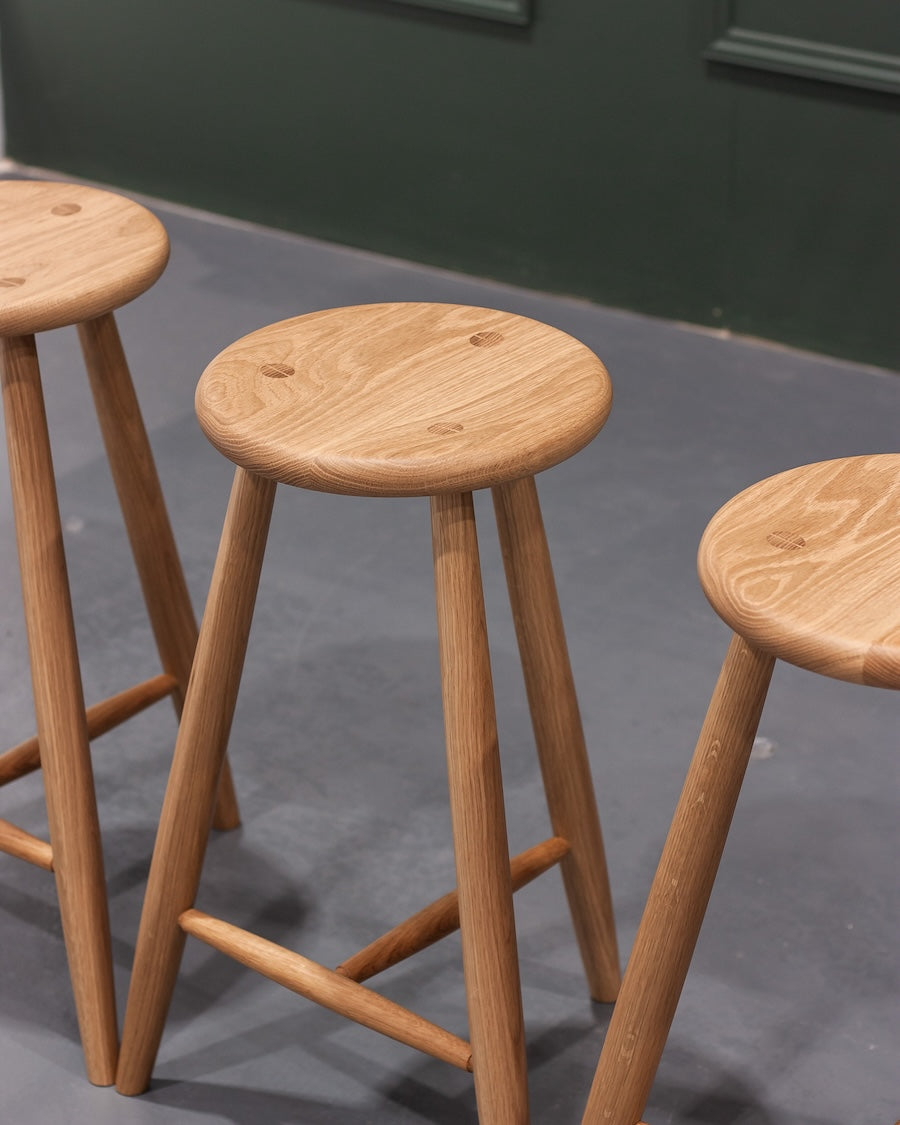 Three wooden stools with round seats and thin legs on a gray floor.